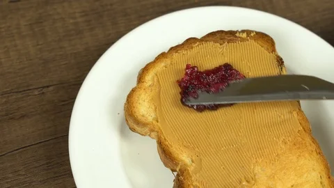 Spreading strawberry jam on top of peanut butter bread Stock Footage 113074907