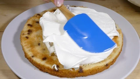 Spreading thick cream onto a layer of sponge cake. Vídeos de archivo 121780057