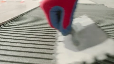Spreading tile adhesive on the floor with a notched trowel. A construction Stock Footage 341072415
