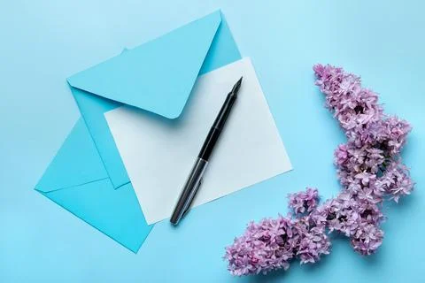 Spring branches of lilac and an envelope with a blank for text on a blue back Stock Photos
