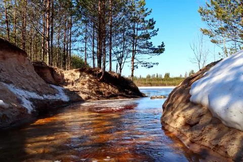 Spring creek between two steep sandy banks with snow Stock Photos
