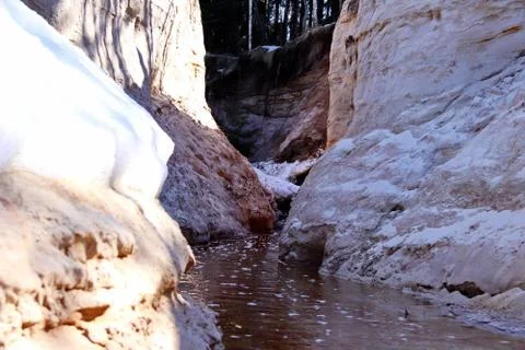 Spring creek between two steep sandy banks with snow Foto stock