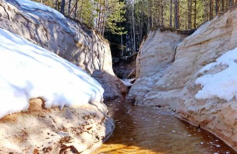 Spring creek between two steep sandy banks with snow Stock Photos