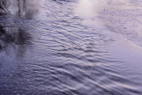 Spring creek flows through the asphalt road. Stock Photos