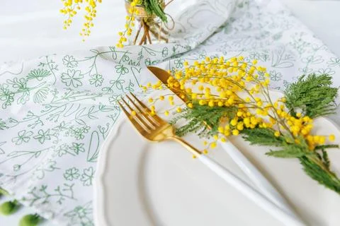 Spring dining table with golden cutlery and mimosa bouquet Stock Photos