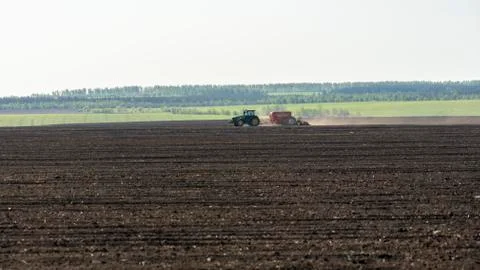 Spring field work, the tractor sows wheat in the field on the background of g Stock Photos