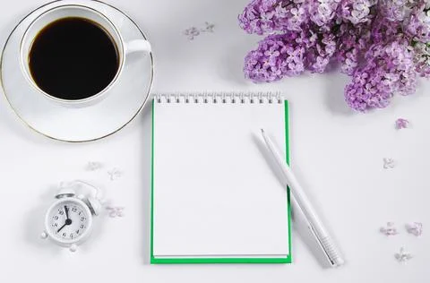 Spring flatlay. Notepad, lilac flowers and cup of coffee on light background. Stock Photos