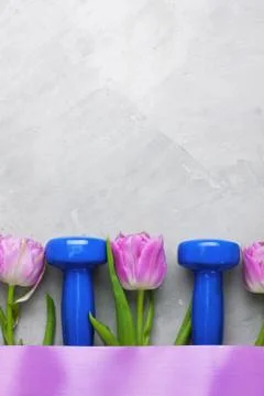 Spring flatlay sports composition with blue dumbbells and purple tulips. Stock Photos