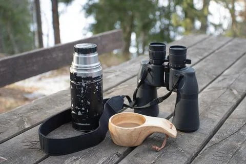 Spring forest. On the table are binoculars, a thermos and mugs of coffee. Stock Photos