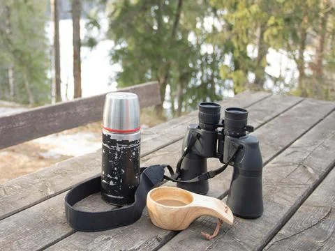 Spring forest. On the table are binoculars, a thermos and mugs of coffee. Stock Photos