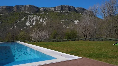 Spring. House with pool in the mountains. Man mowing the lawn. Lawn mower Stock Footage 129503566