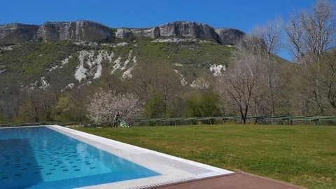 Spring. House with pool in the mountains. Man mowing the lawn. Lawn mower Stock Footage 129503568