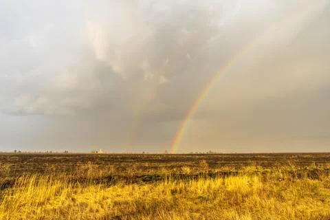 Spring landscape with double rainbow over burned field after thunderstorm. Be Stock Photos
