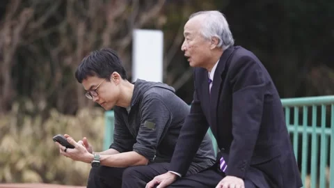 In a spring park, a man in his 70s in a suit and a man in his 30s sit on a bench Vídeo Stock 307735151