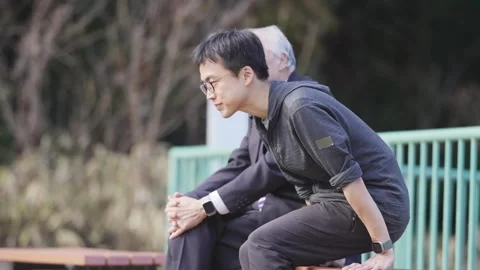 In a spring park, a man in his 70s in a suit and a man in his 30s sit on a bench Stock Footage 307737155