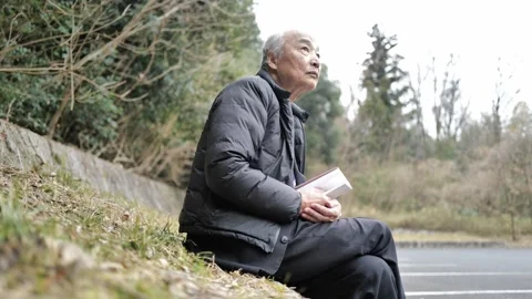 In a spring park, a man in his 70s wearing a suit and down jacket sits by a 動画素材 307793941