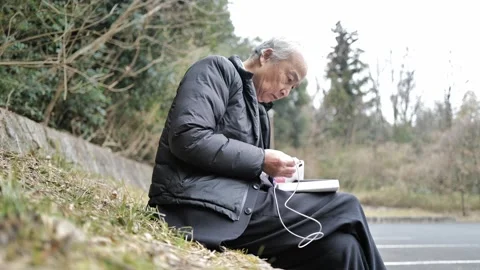In a spring park, a man in his 70s wearing a suit and down jacket sits by a 動画素材 307794515