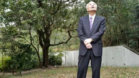 In a spring park, a man in his 70s wearing a suit stands at a corner, holding a Stock Footage 307794894
