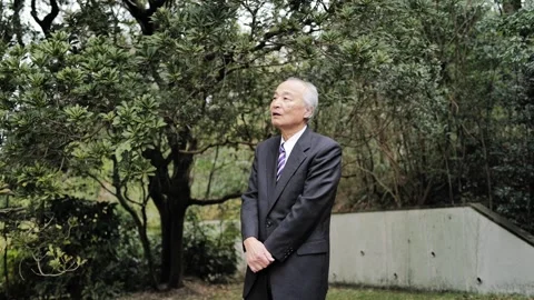In a spring park, a man in his 70s wearing a suit stands at a corner, holding a 스톡 동영상 307795121