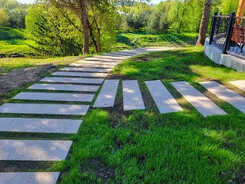 In the spring park, a path made of concrete rectangles is laid between the .. 库存照片