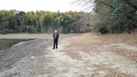 In a spring park with a pond and bamboo grove, a man in his 70s in a suit and Stock Footage 307796009
