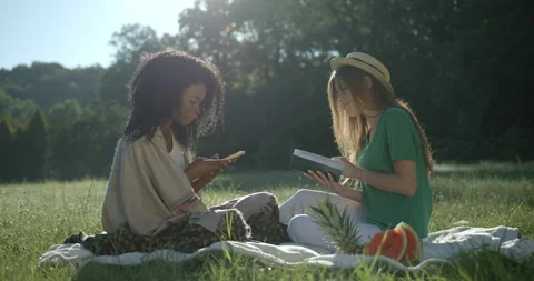 Spring picnic of two mixed race girlfriends on the meadow. The blonde caucasian Stock Footage 233925341