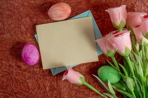 Spring roses and vibrant Easter eggs with a blank card on a rustic background Foto stock