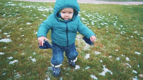 Spring. Steadicam shot of kid running down the sidewalk, grass and melting snow Video stock 83478691