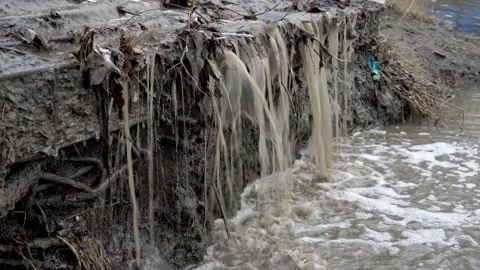 Spring stream of dirty water flows into the river on a stone drain as a waterfal Video stock 124868771
