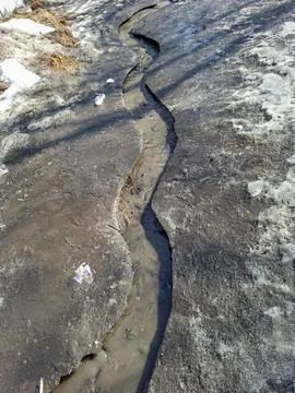 Spring stream flows through melting ice in early season Fotos Stock