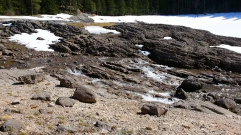 Spring stream flows through  stone to  frozen lake 스톡 동영상 74075420