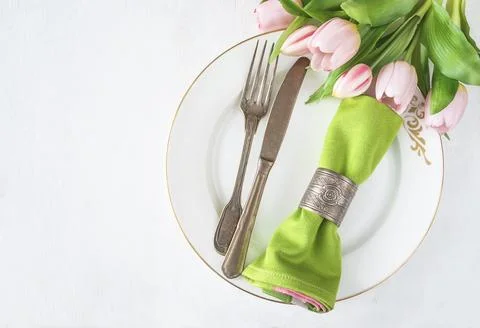 Spring table setting; Bouquet of pink tulips, vintage fork and knife, green.. Stock Photos