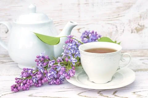 Spring tea time still life. White cup of tea, tea pot and bunch of purple l.. Stock Photos