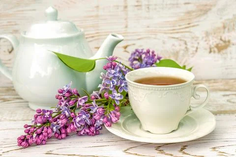 Spring tea time still life. White cup of tea, tea pot and bunch of purple l.. Stock Photos