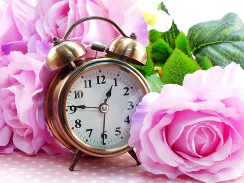Spring time with alarm clock and artificial flowers bouquet background 库存照片