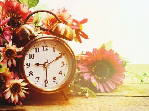 Spring time with alarm clock and artificial flowers bouquet background Stock Photos