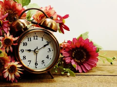 Spring time with alarm clock and artificial flowers bouquet background Stock Photos