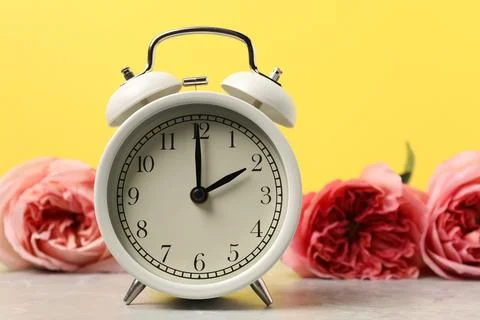 Spring time. Alarm clock and beautiful flowers on grey marble table against.. Stock Photos