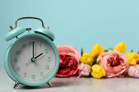 Spring time. Alarm clock and beautiful flowers on grey marble table against.. 写真素材