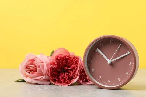 Spring time. Alarm clock and beautiful roses on grey marble table against y.. 스톡 사진