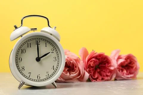 Spring time. Alarm clock and beautiful roses on grey marble table against y.. 写真素材