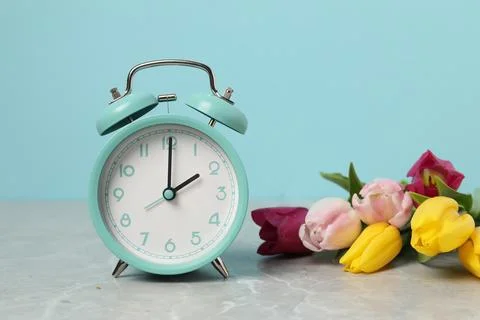 Spring time. Alarm clock and beautiful tulips on grey marble table against .. 写真素材