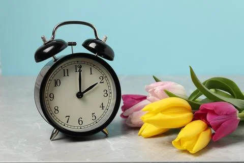 Spring time. Alarm clock and beautiful tulips on grey marble table against .. 스톡 사진