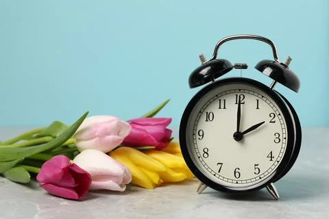 Spring time. Alarm clock and beautiful tulips on grey marble table against .. 写真素材