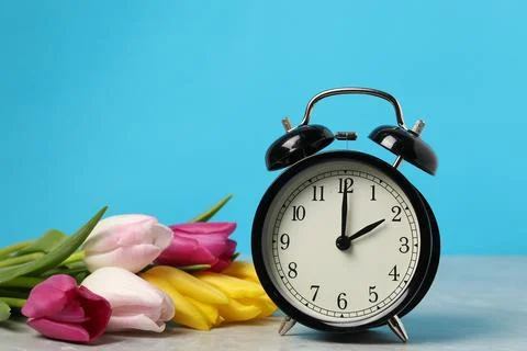 Spring time. Alarm clock and beautiful tulips on grey marble table against .. 写真素材