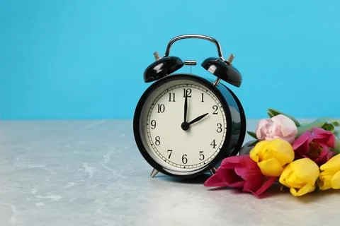 Spring time. Alarm clock and beautiful tulips on grey marble table against .. Stock Photos