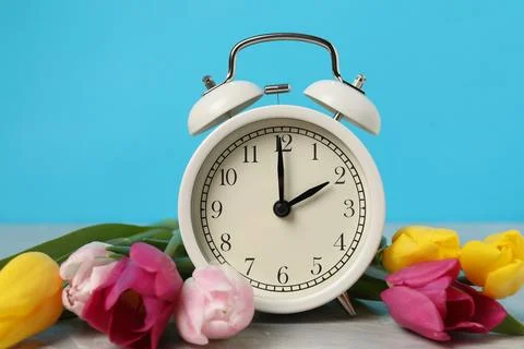 Spring time. Alarm clock and beautiful tulips on grey marble table against .. Foto stock