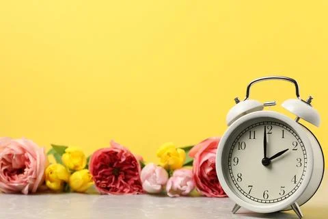 Spring time. Alarm clock and beautiful flowers on grey marble table against.. Stock Photos