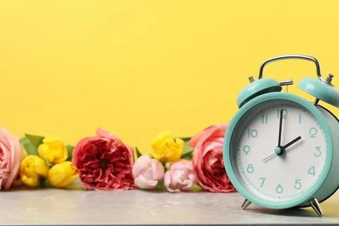 Spring time. Alarm clock and beautiful flowers on grey marble table against.. Foto stock