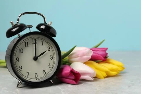 Spring time. Alarm clock and beautiful tulips on grey marble table against .. 写真素材